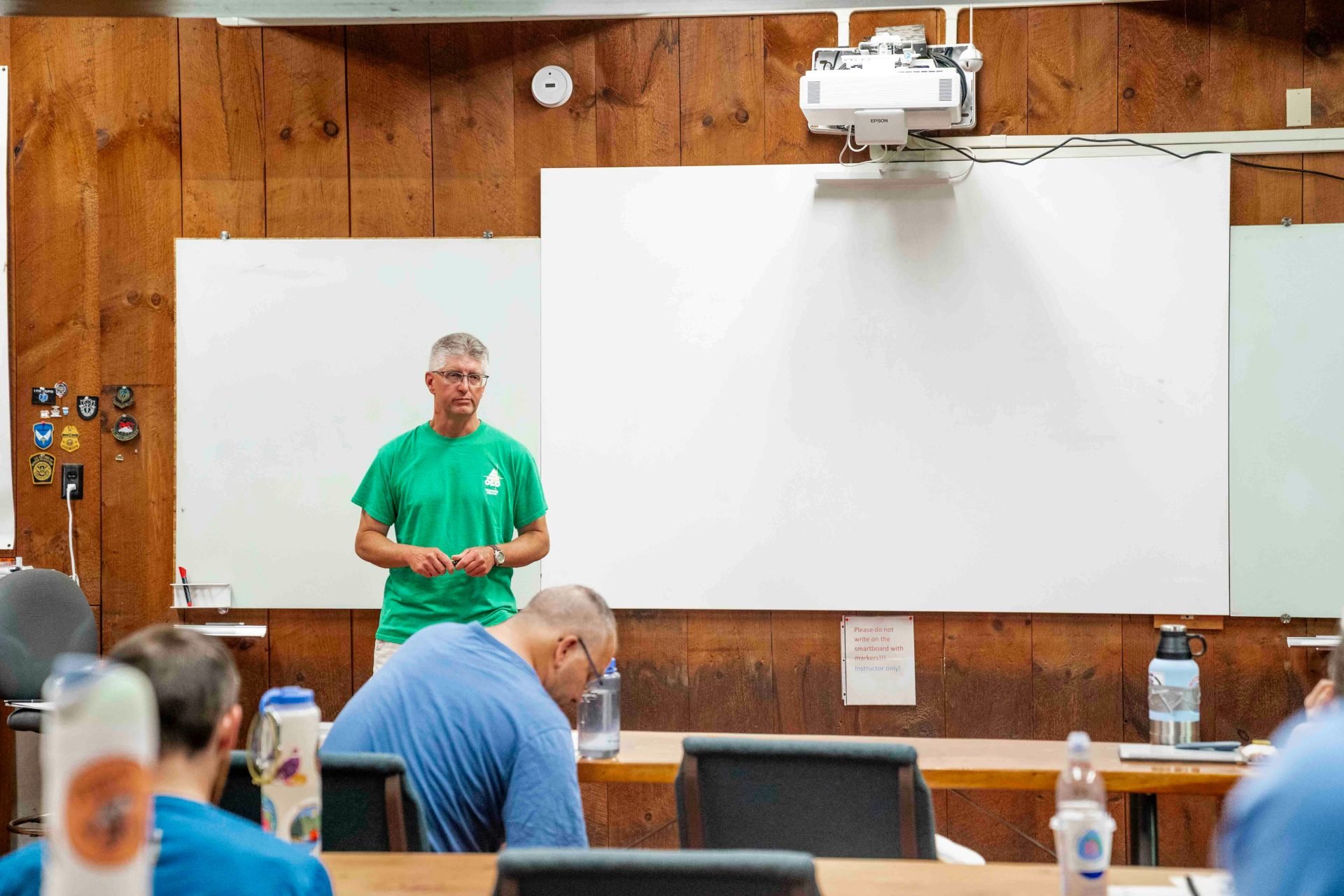 Man in green shirt presents to audience in classroom.