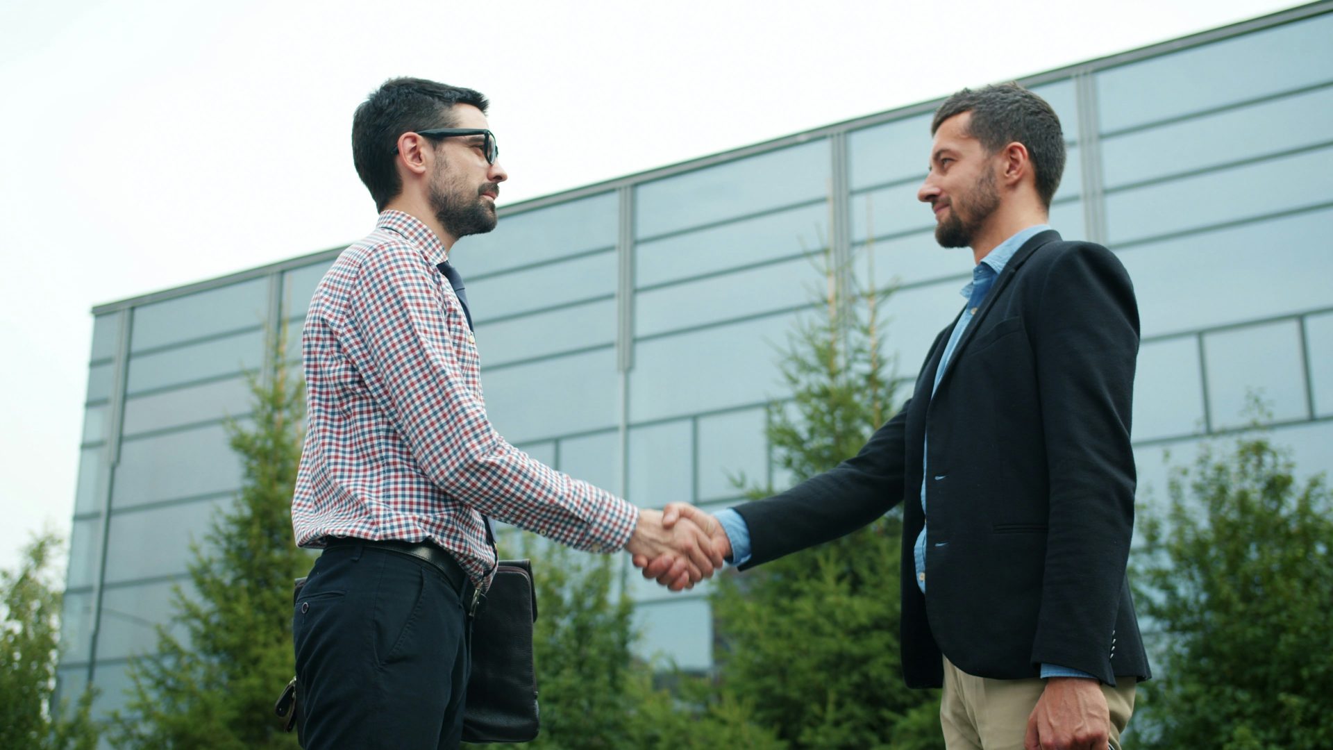 Two businessmen shaking hands outside modern building